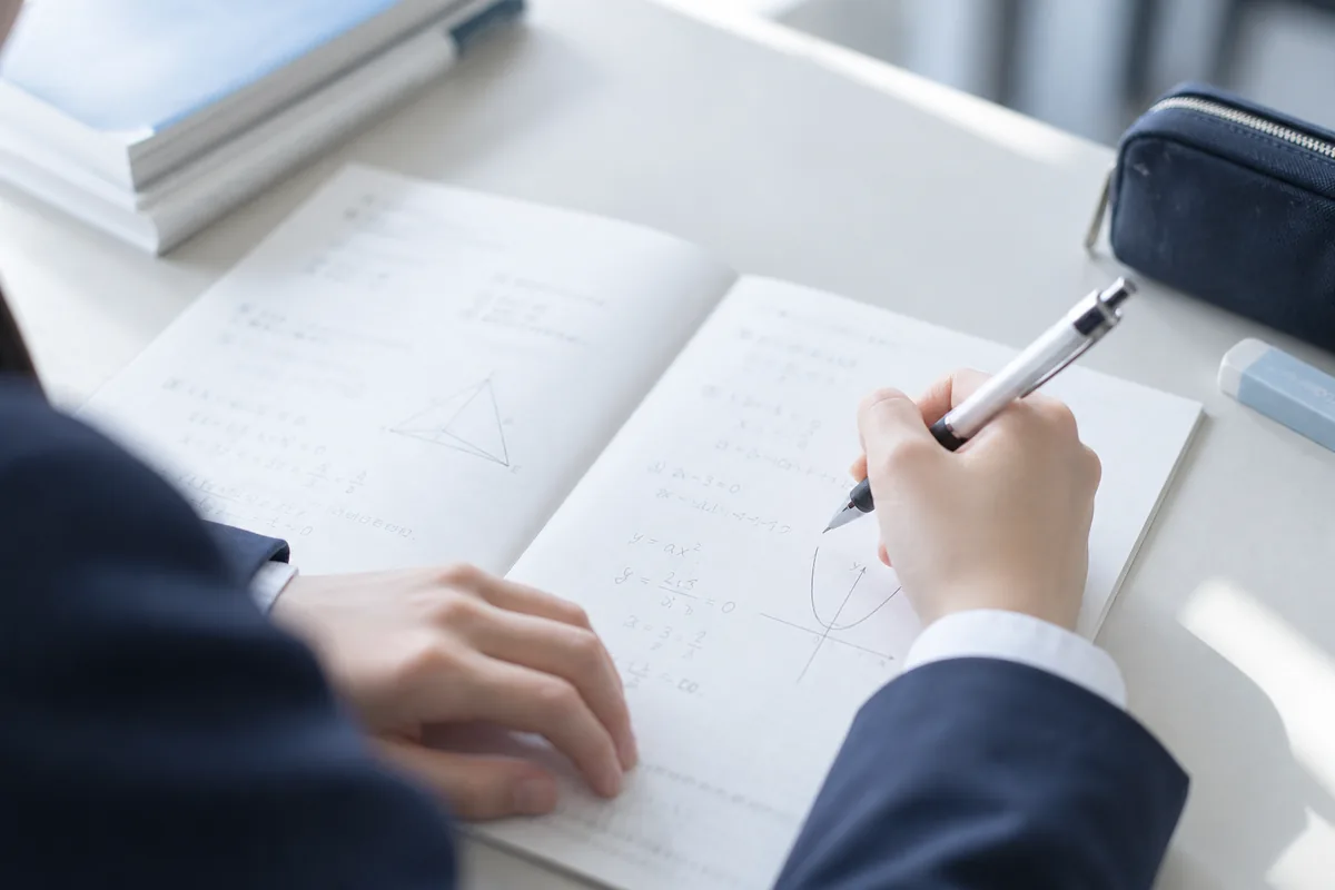 数学の問題が書かれたノートに解答を書き込む生徒の手元
