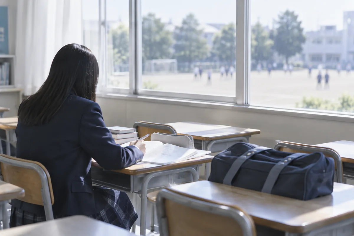 窓際の席で自習に取り組む生徒の後ろ姿と机の上のバッグ